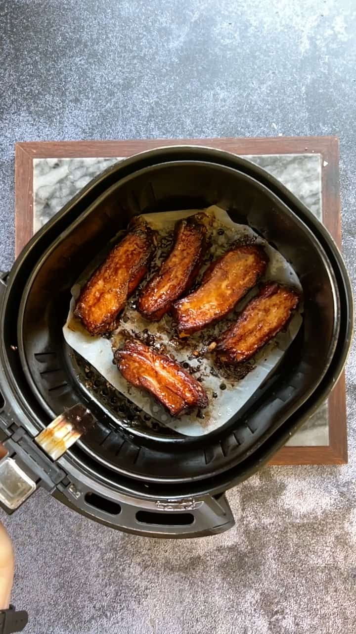 A person is using an air fryer to cook pork belly.