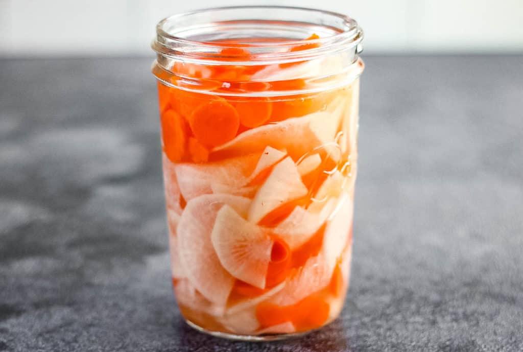 low angle shot of a jar of pickled daikon radish and carrots.