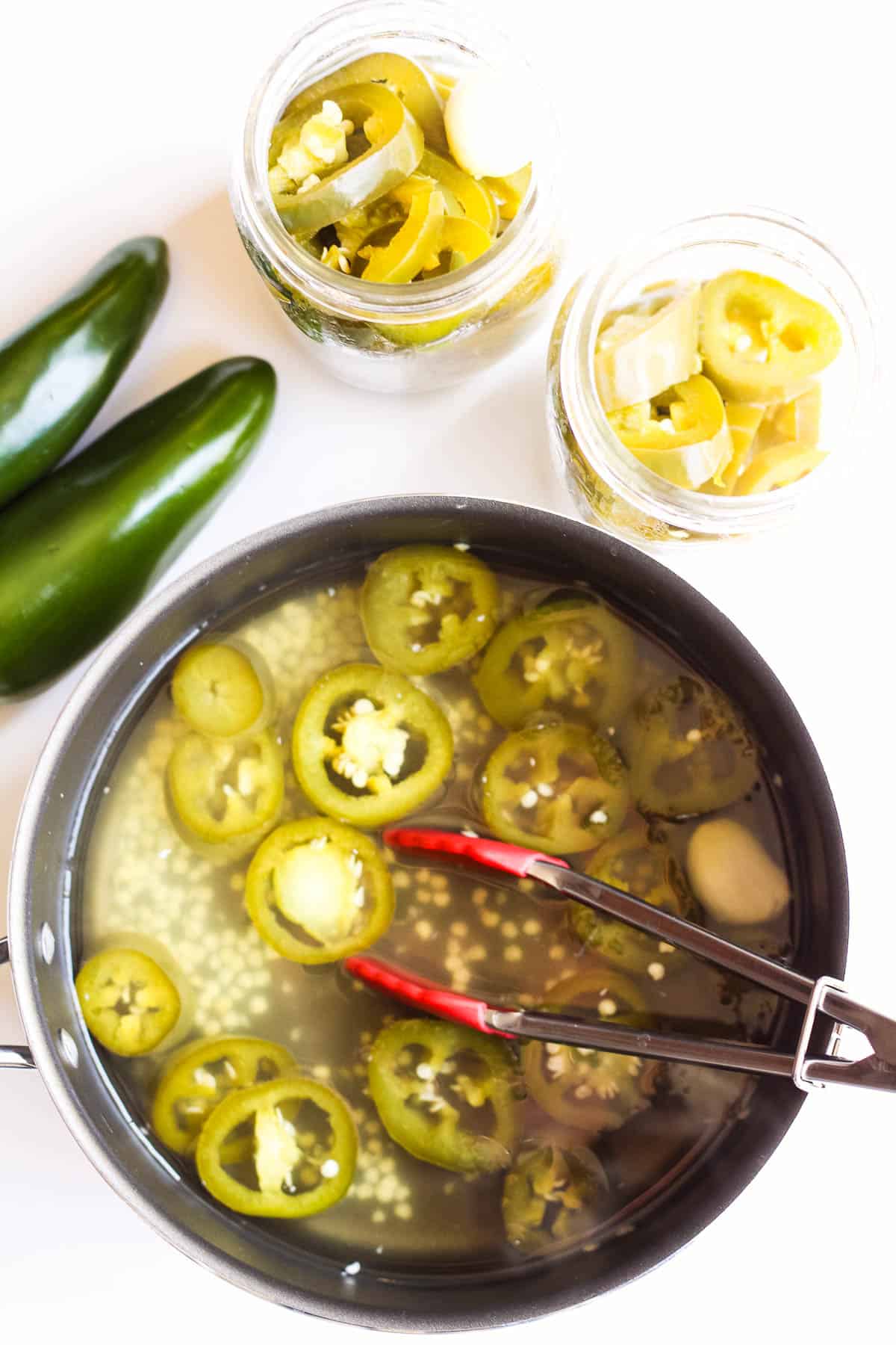 A pot filled with pickled jalapenos and jars of pickles.