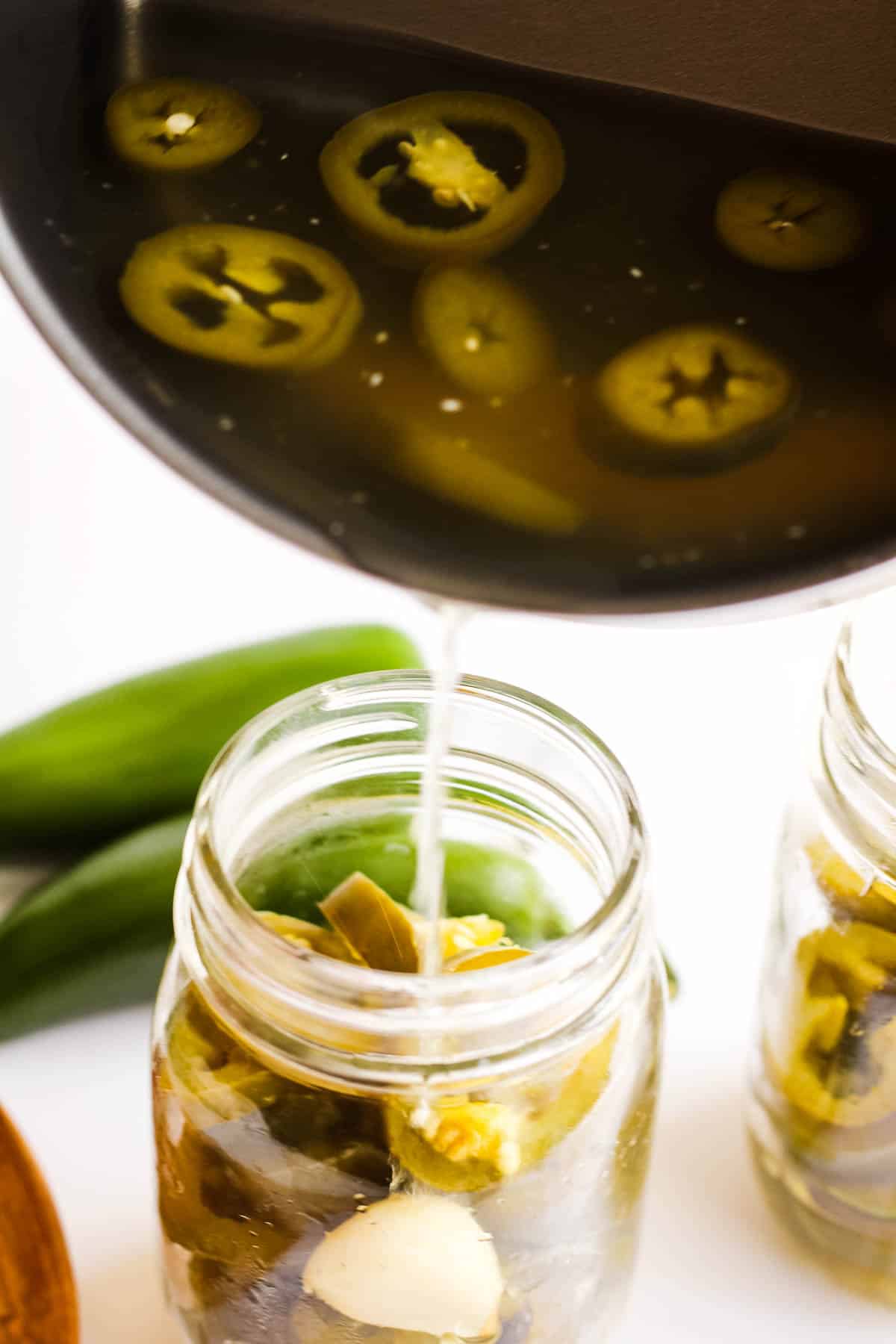 A jar of pickled jalapenos being poured into a pan.