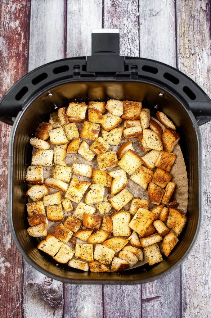 An air fryer loaded with croutons on a wooden table.