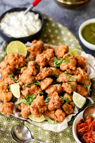 High angle shot of a platter of chicken pakora garnished with lime wedges.