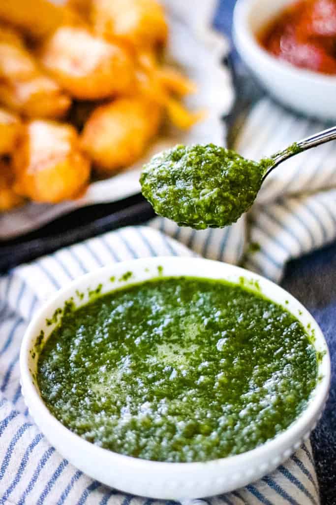 high angle shot of a bowl of cilantro mint chutney with a spoonful being lifted above the bowl.