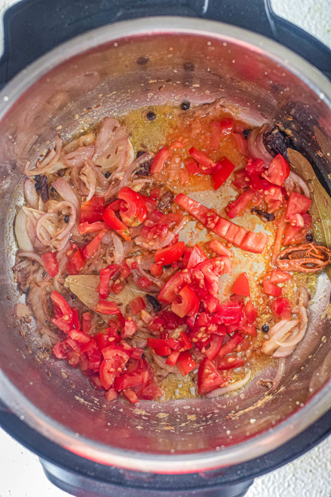 An instant pot filled with tomatoes and onions, cooking shrimp biryani.