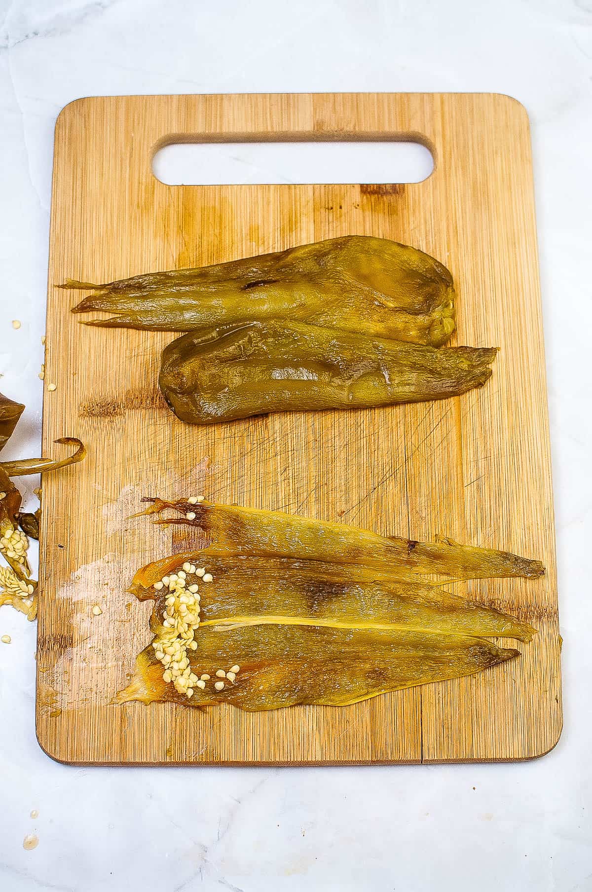 A wooden cutting board with two pieces of octopus and air fryer roasted hatch chiles on it.