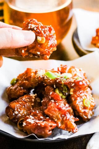 low angle shot of air fryer korean fried chicken. There is a hand holding a piece of the chicken.