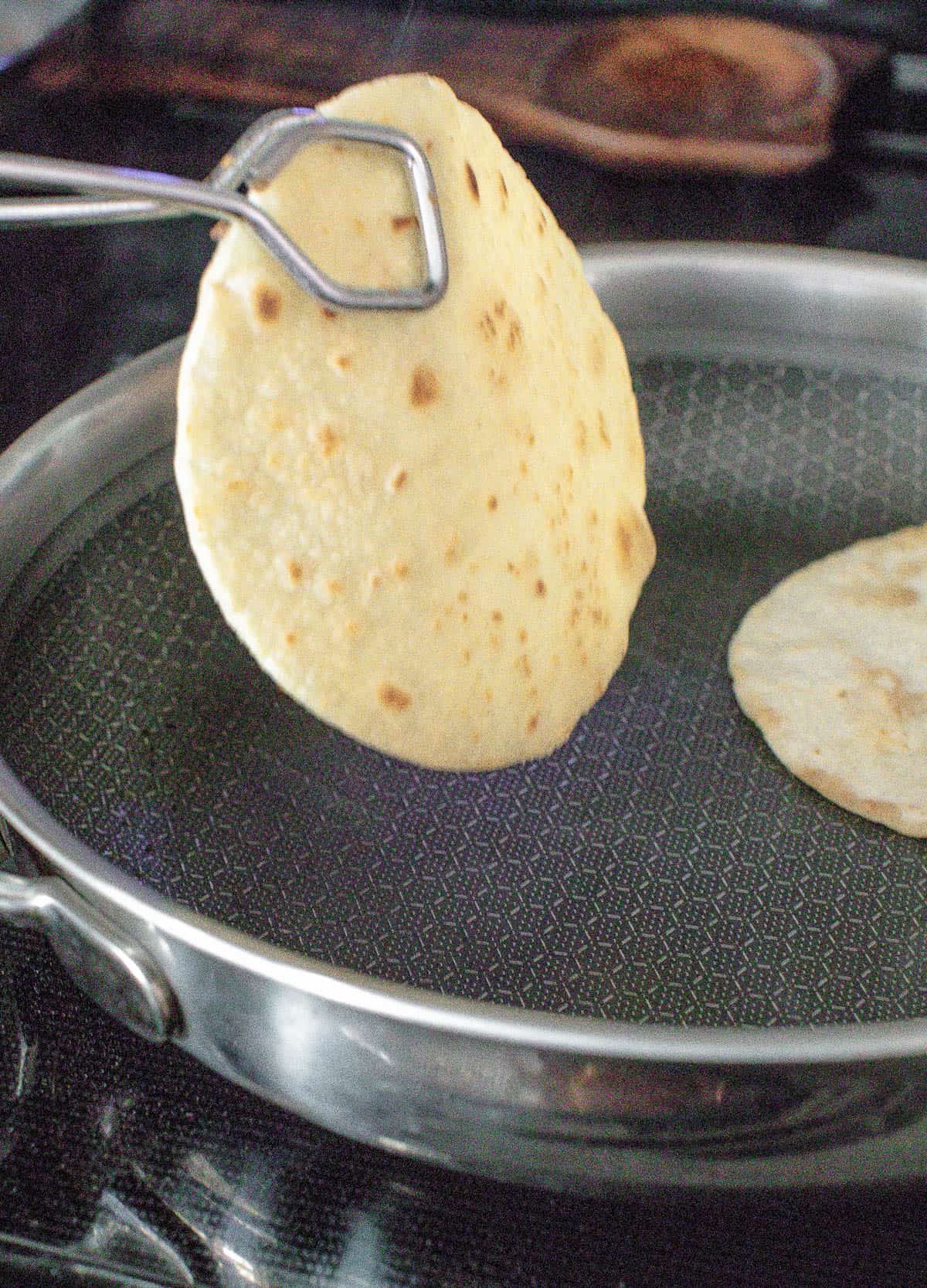 A tortilla is being pulled out of a pan to create flavorful blackened mahi mahi tacos.
