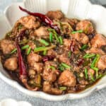 Mongolian chicken in a white bowl with green chilies.