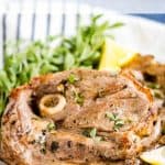 A plate with succulent air fryer lamb chops garnished with herbs and lemon wedges, accompanied by a side of greens. Text above reads "Air Fryer LAMB CHOPS," and below reads "allwaysdelicious.com.