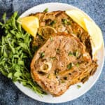 Overhead shot of an air fried lamb chop with fresh oregano and lemon wedges.