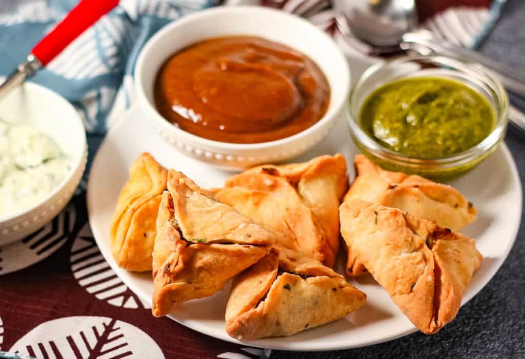 Low-angle shot of air fried samosas on a plate with tamarind chutney and cilantro mint chutney.
