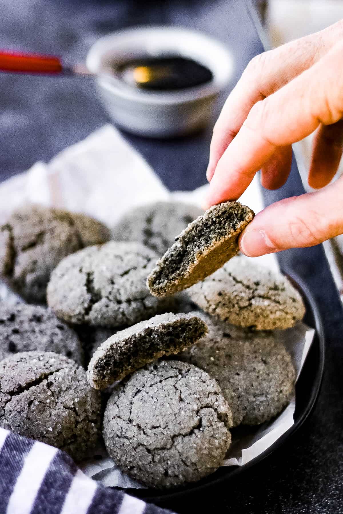 low angle shot of black sesame cookies. There is a hand lifting a half cookie.
