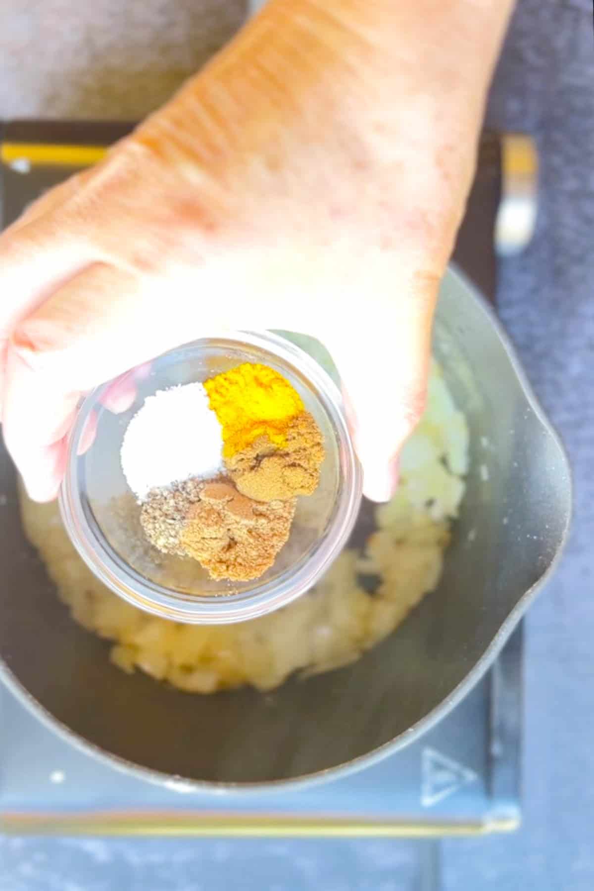 A person adding spices to a pot of chana aloo masala on a stovetop.