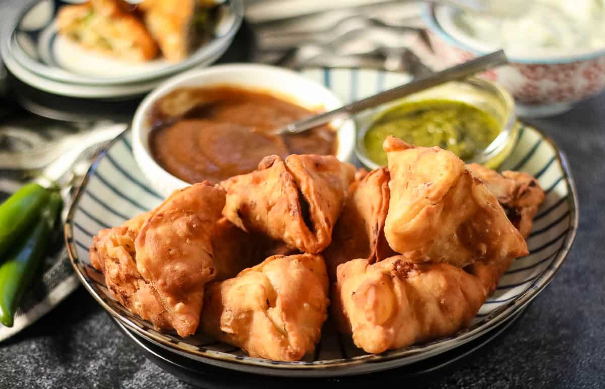 Low angle shot of a plate of samosas with chutney dipping sauces.