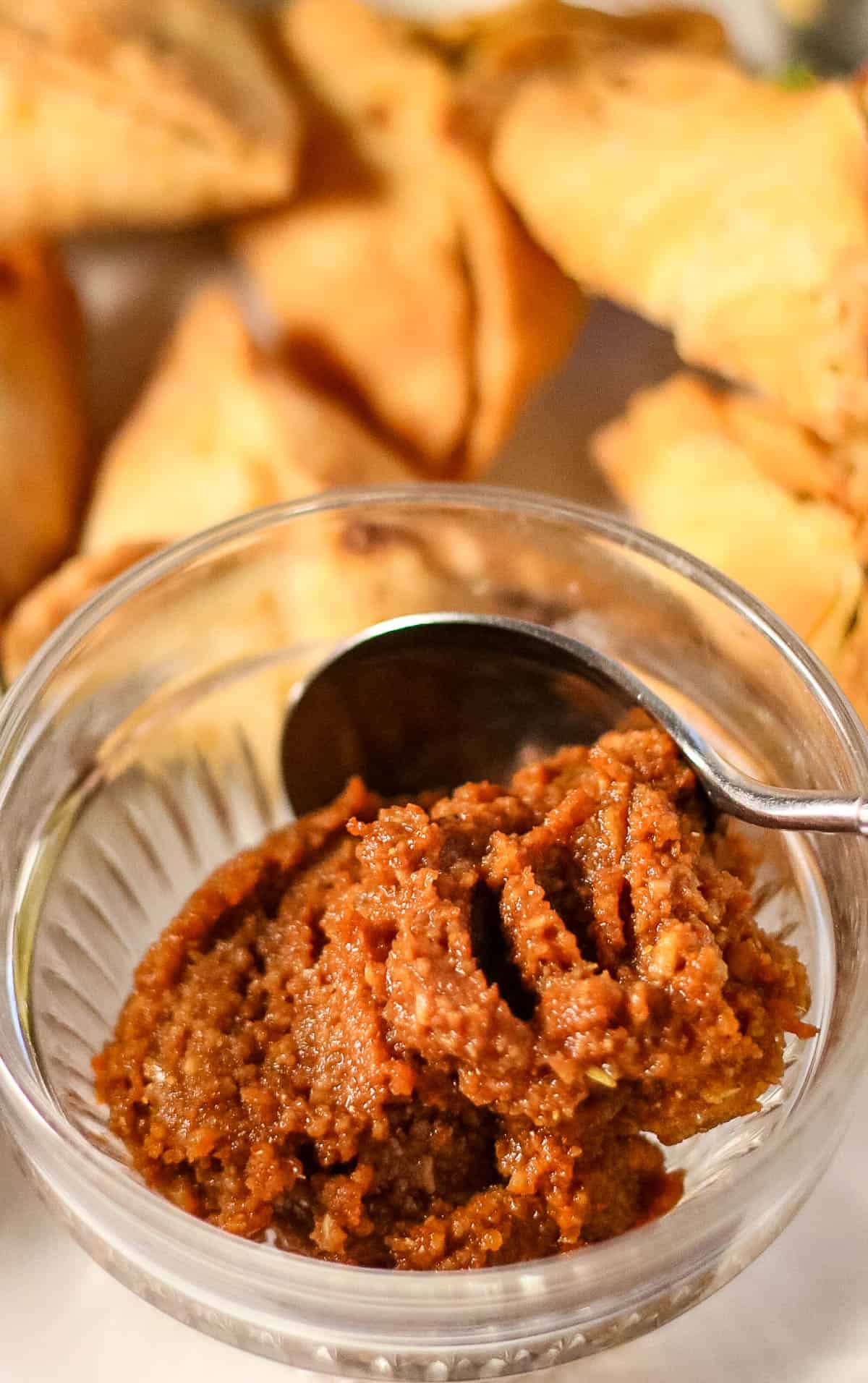 High angle shot of a bowl of garlic chutney with samosas in the background.