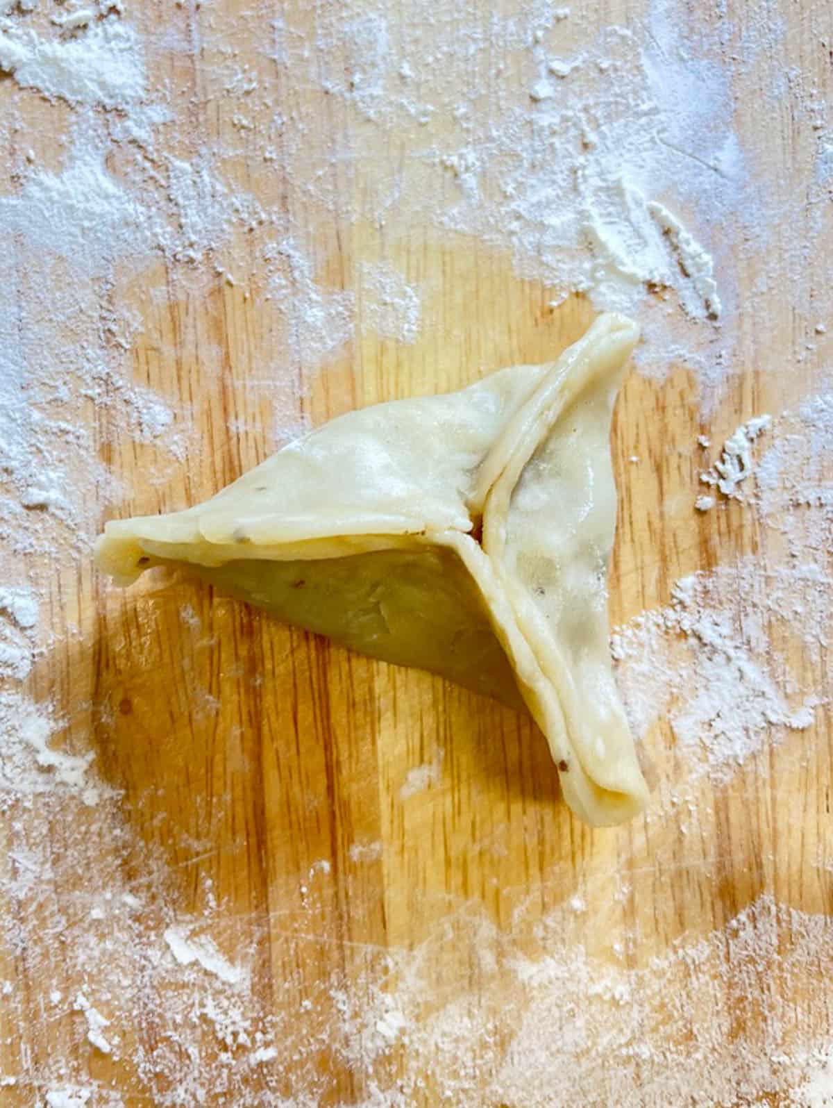 A triangle-shaped dumpling resembling an onion samosa, resting on a cutting board.
