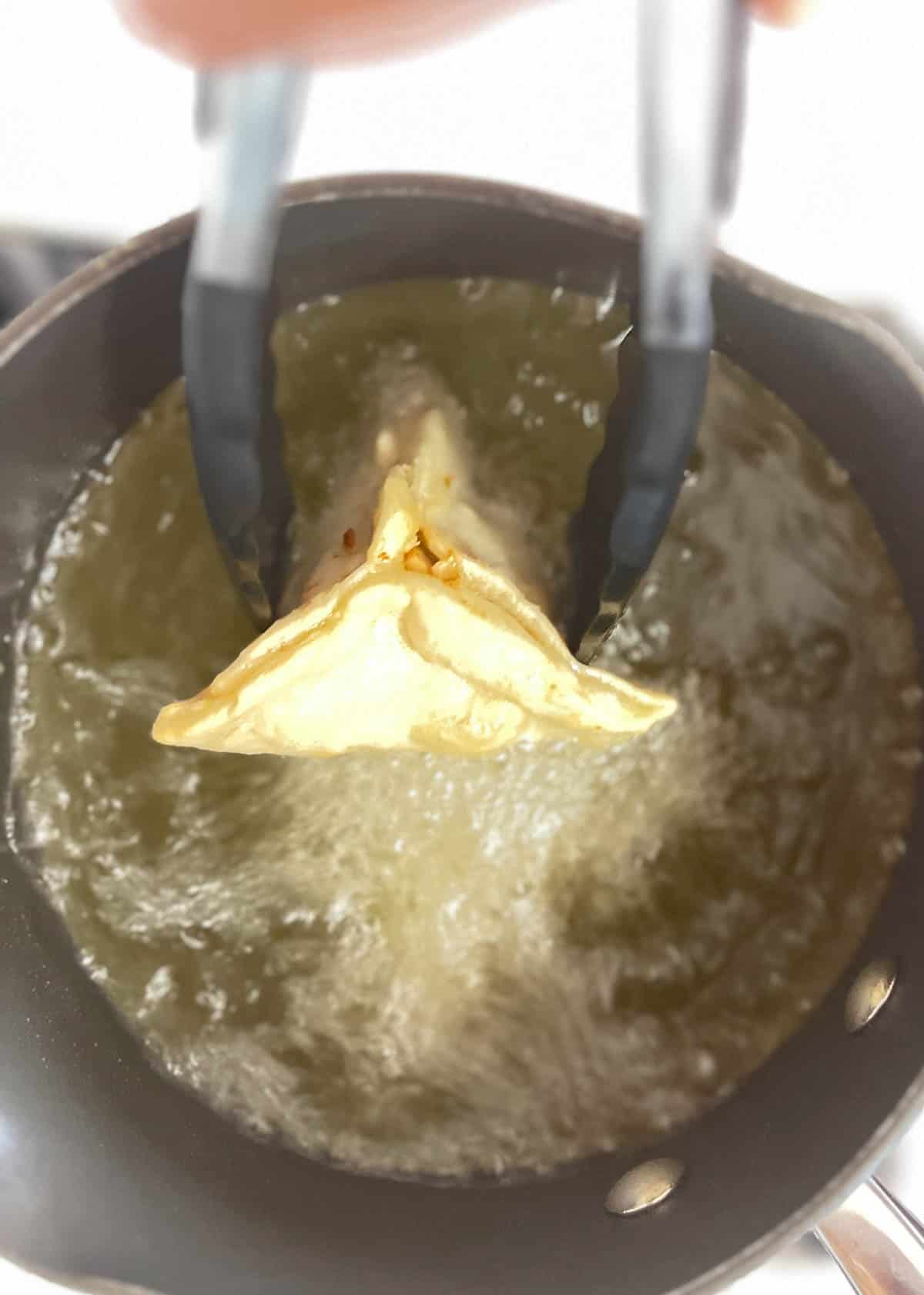 A person frying onion samosas in a pan.