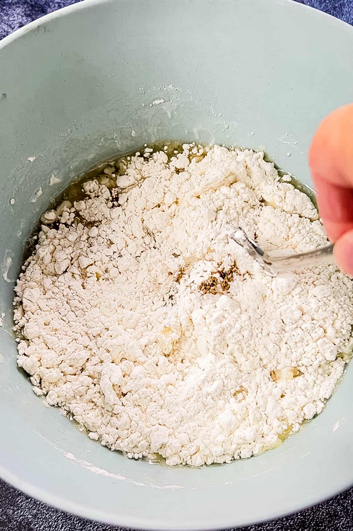 A person mixing flour in a bowl with a spoon while preparing air fryer samosas.