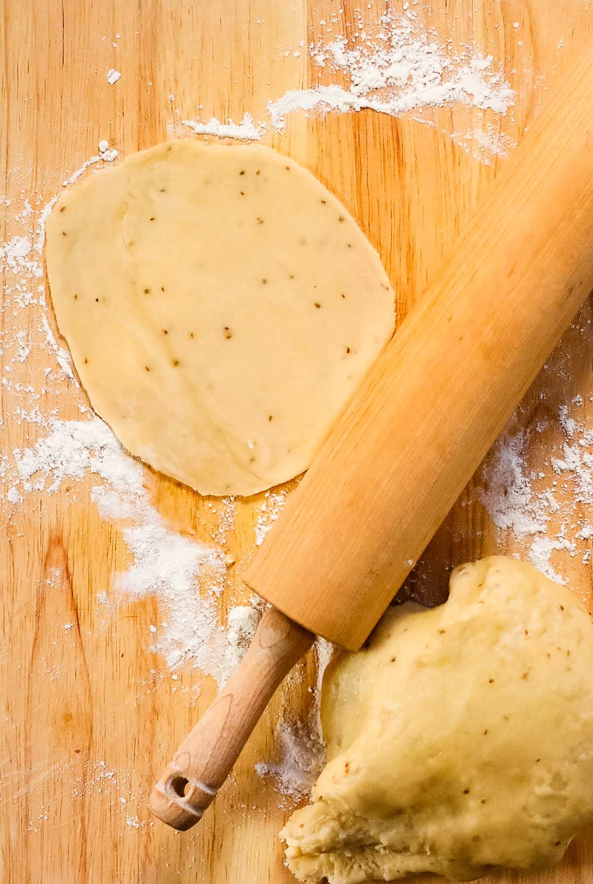 A rolling pin and dough on a wooden cutting board preparing air fryer samosas.