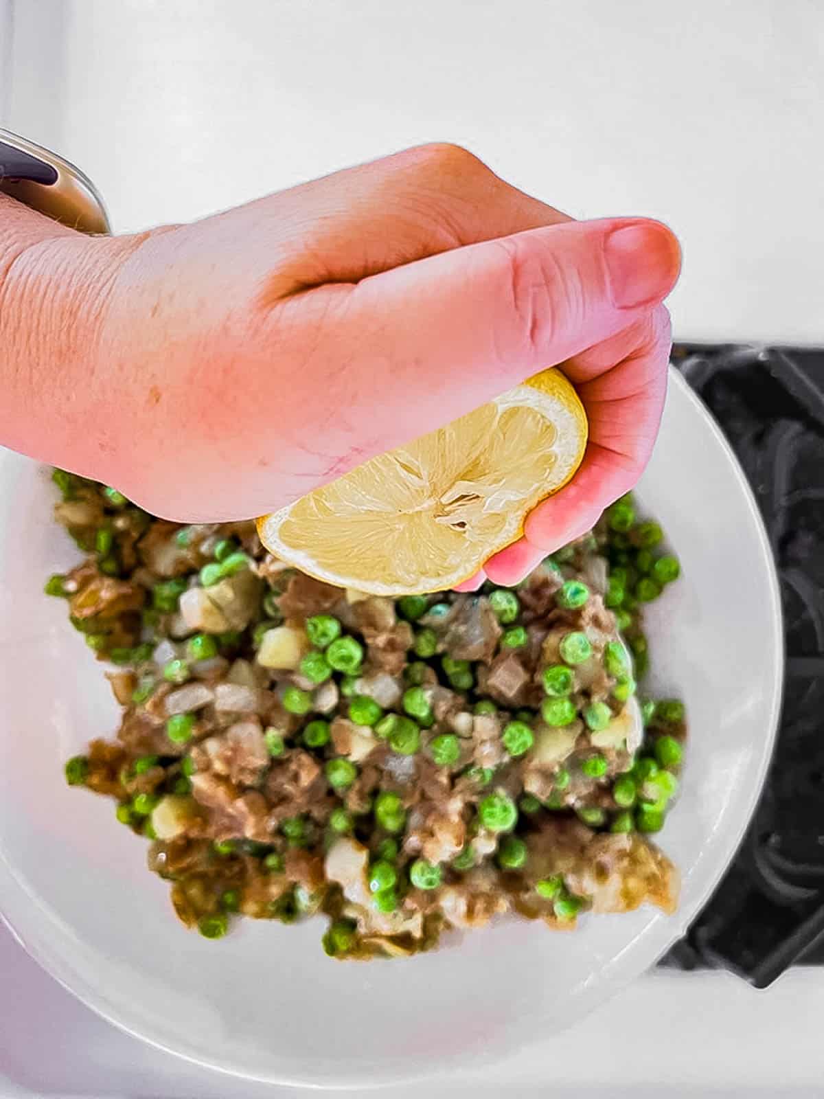 A person garnishing a plate of peas with freshly squeezed lemon juice.