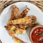 Plate of air fryer zucchini fries served with a side of marinara sauce on a charming woven placemat.