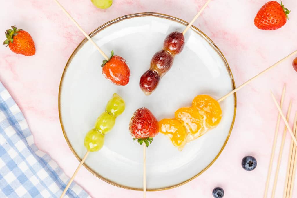 A plate of tanghulu fruit skewers on a pink background.