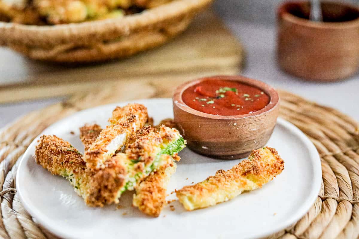 Low angle shot of zucchini fries on a white plate with ketchup on the side.