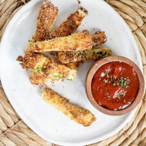 Overhead shot of zucchini fries on a white plate with a bowl of ketchup.