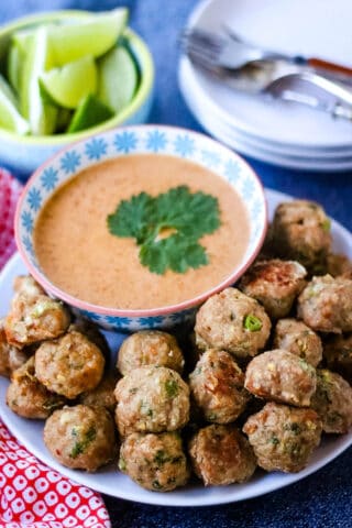 Hi angle shot of a serving platter piled with Thai turkey meatballs with a bowl of red curry coconut dipping sauce.