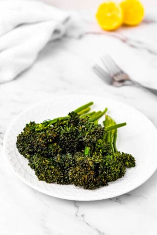 High angle shot of a plate of air fryer broccolini with lemon and forks in the background.