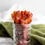 Low angle shot of candied bacon in a mason jar with a green napkin behind.