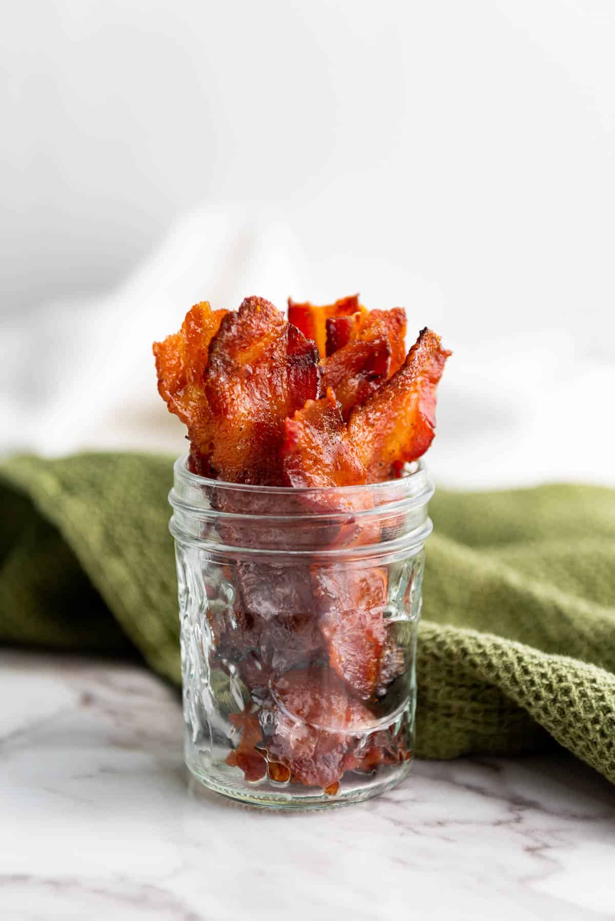 Low angle shot of candied bacon in a mason jar with a green napkin behind.