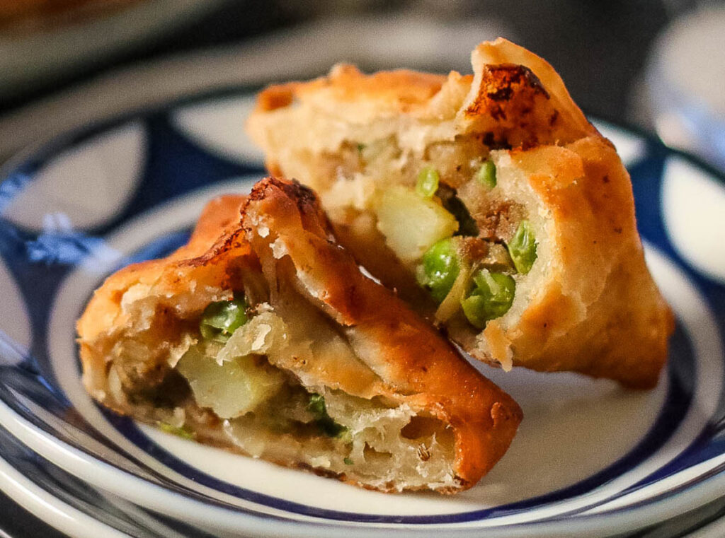 Low angle shot of a fried samosa with potato and pea filling. The samosa is cut in half so you can see the inside.
