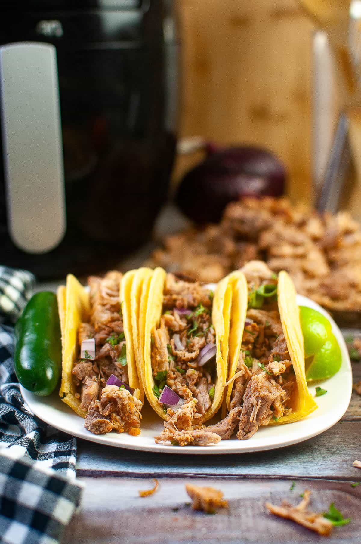 Low angle shot of carnitas tacos with carnitas meat and an air fryer in the background.