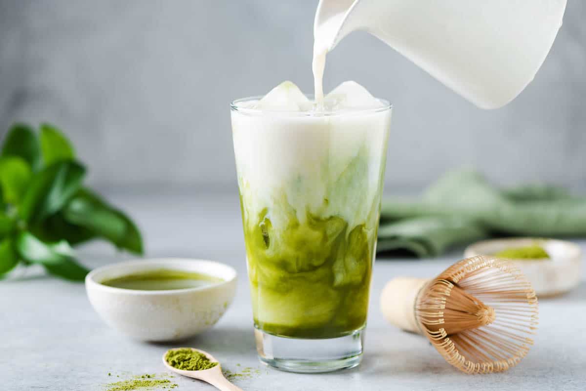 Low angle shot of a glass of iced matcha milk tea with milk being poured into the glass.