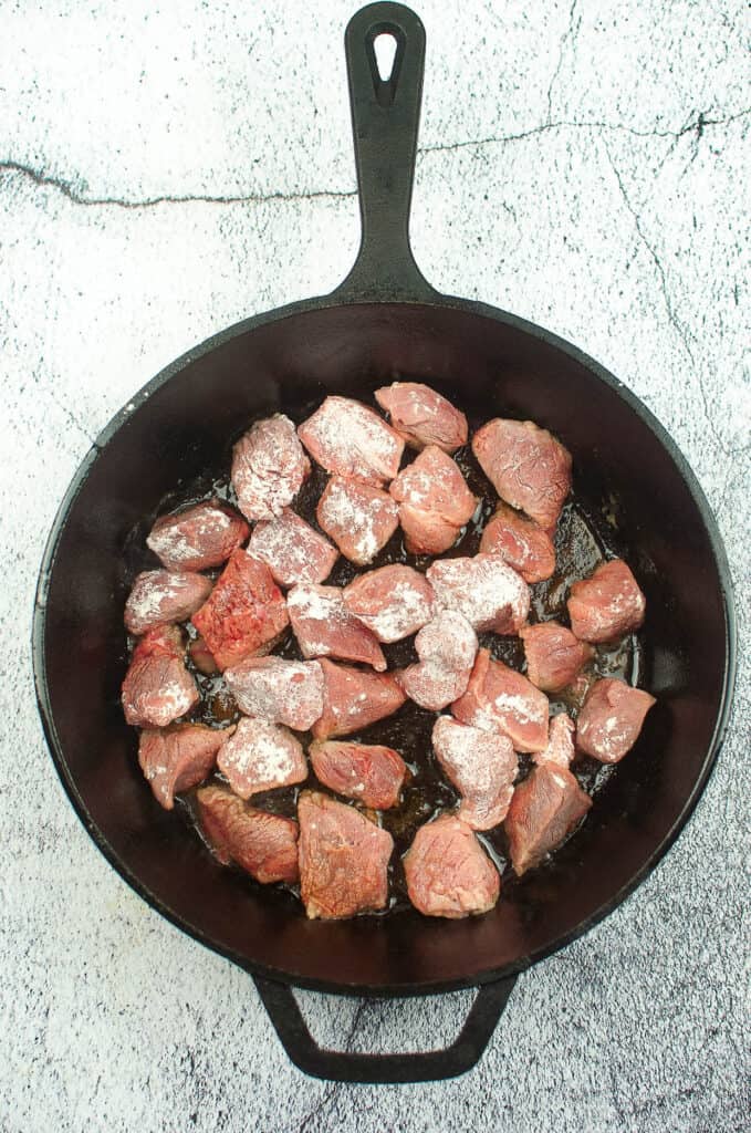 beef stew chunks browning in a cast iron skillet.
