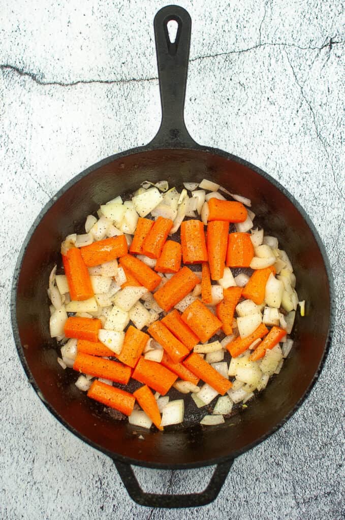 onions and carrots sauteeing in a cast-iron skillet.