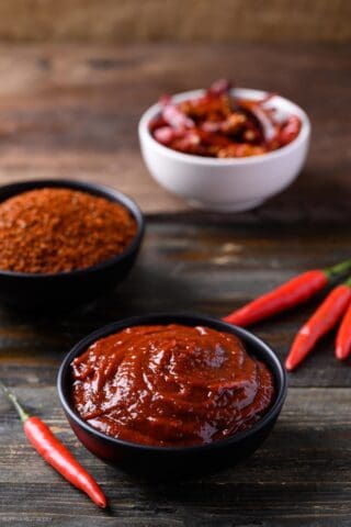 Gochujang in a bowl with a bowl of gochugaru, fresh red chiles, and dried red chiles.