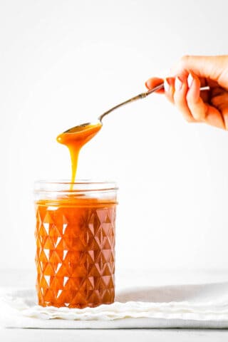 A jar of miso caramel with a hand lifting a spoonful of the caramel out of the jar.