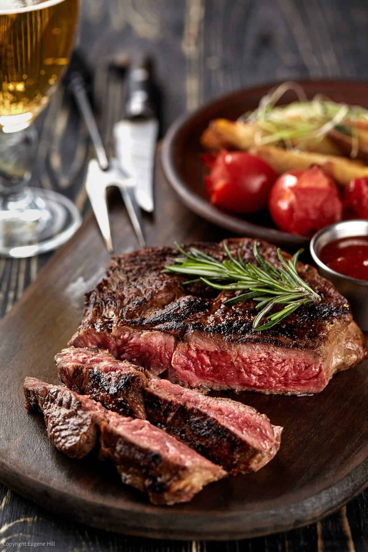 High-angle shot of a medium-rare steak, sliced, with fresh rosemary sprig on top. Image credit: Depositphotos.