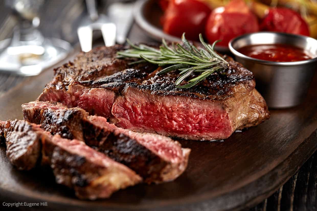 Medium-rare steak, sliced, with fresh rosemary sprig on top. Image credit: Depositphotos.