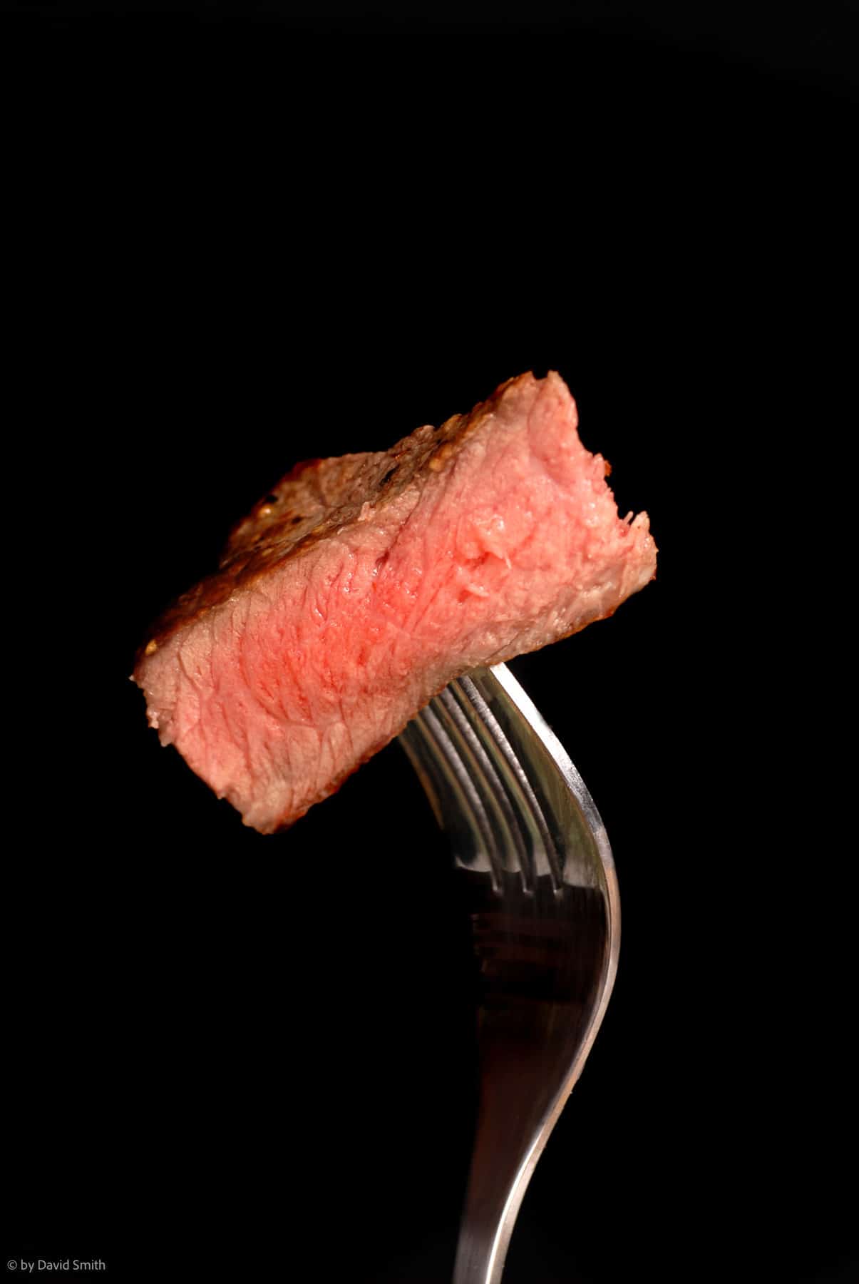 Fork holding a piece of medium-rare steak in the air. Image credit: Depositphotos.