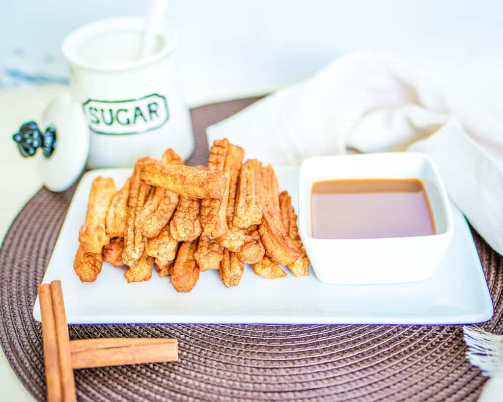 Air fryer churros on a white plate with a bowl of caramel sauce.