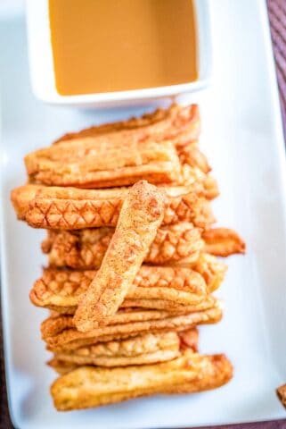 Air fryer churros on a white plate with a bowl of caramel dipping sauce on the side.