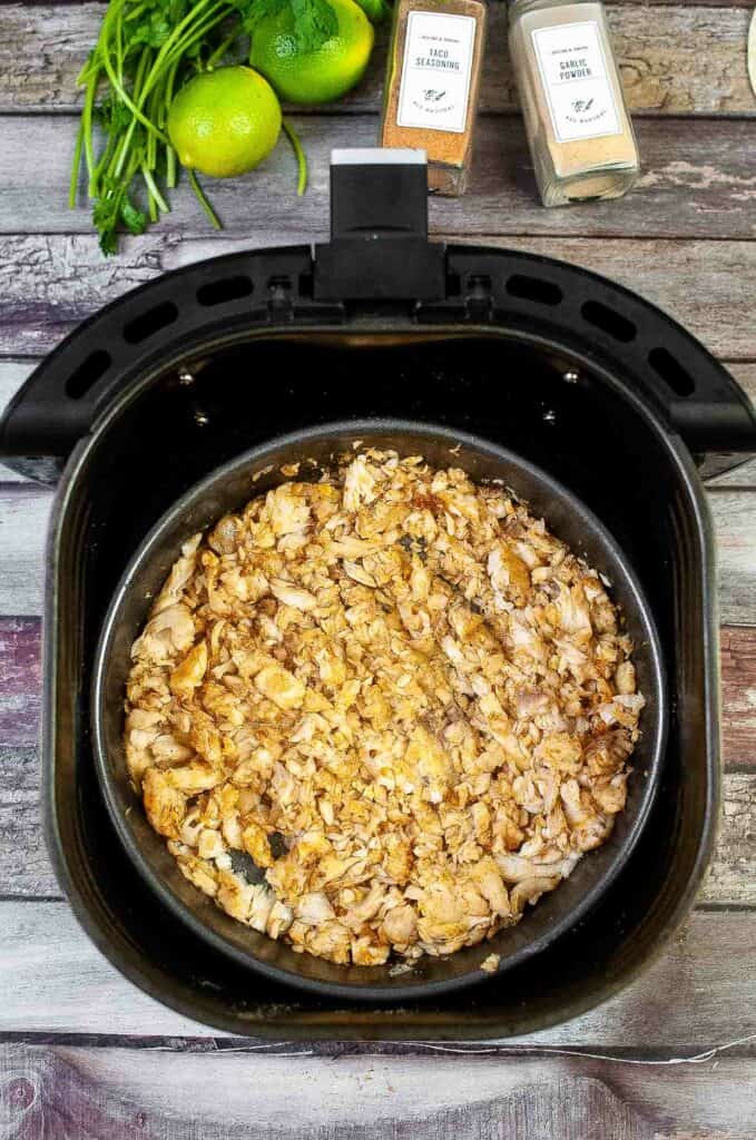 An air fryer filled with shredded chicken and spices, perfect for making fish tacos.
