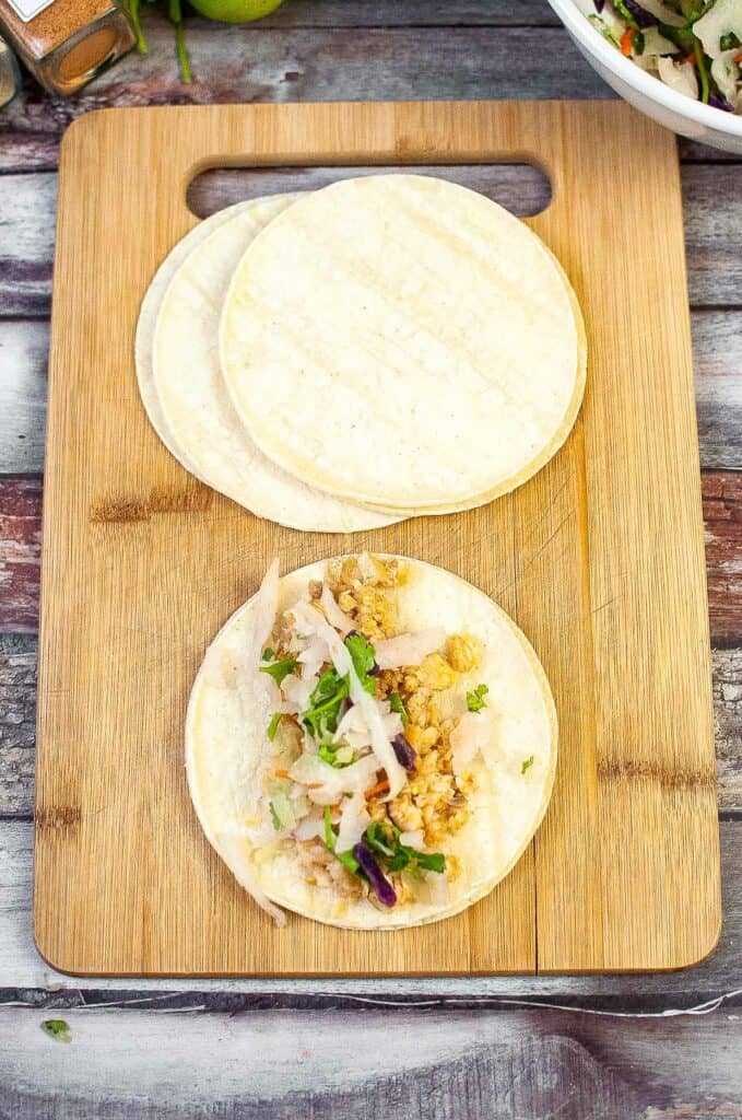 Two air fryer fish tacos perched on a wooden cutting board.