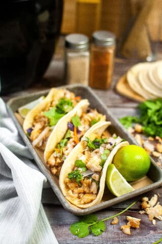 Low angle shot of 3 fish tacos on a small baking sheet with limes.