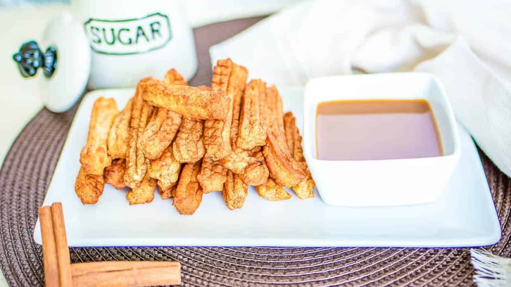 Air fryer churros on a white plate with a bowl of caramel dipping sauce.