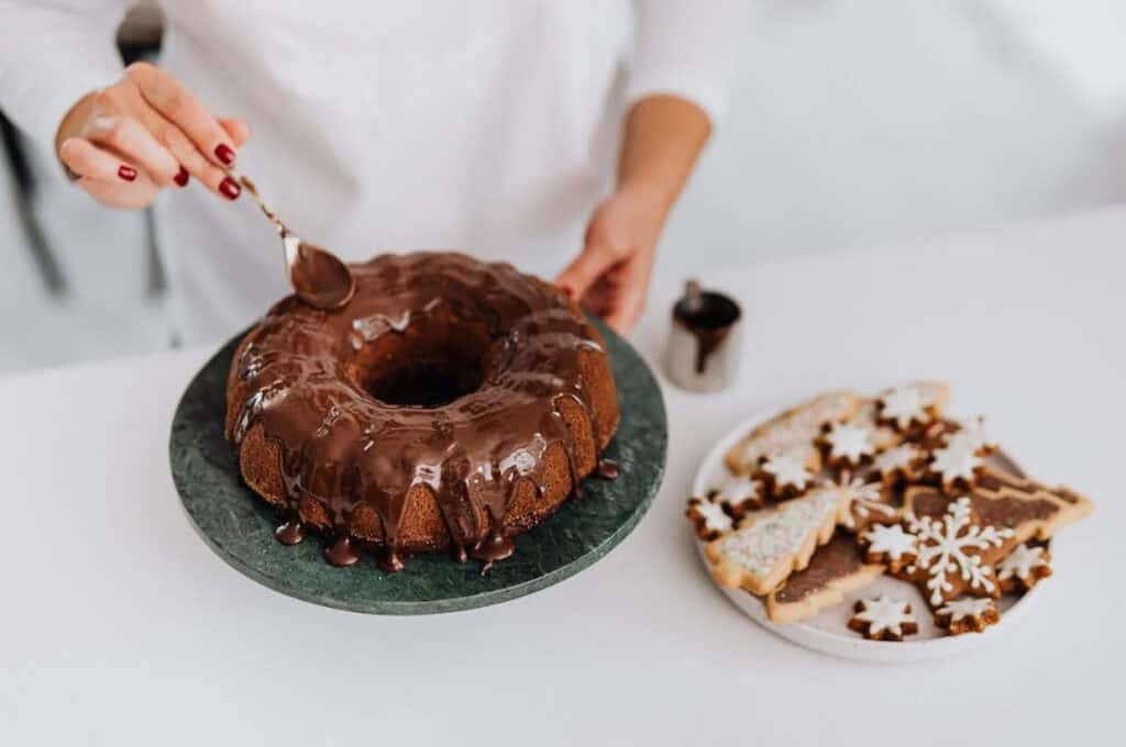 A woman's hands spreading chocolate glaze on a bundt cake.