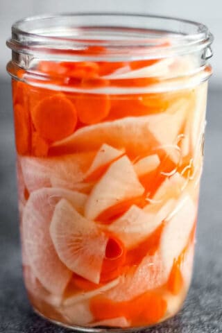 close-up shot of a mason jar filled with pickled daikon radishes and carrots.